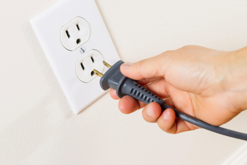 Horizontal photo of female hand inserting power cord receptacle into electric wall outlet